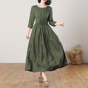 May include: A long, green linen dress with a round neckline and a gathered waist. The dress has 3/4 sleeves and a flowing skirt.