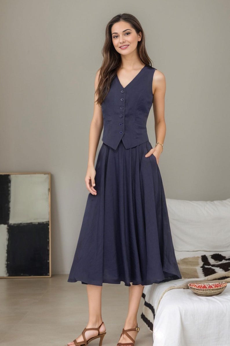 Peut inclure: Un gilet sans manches bleu marine avec un col en V et une fermeture &agrave; boutons, associ&eacute; &agrave; une jupe midi bleu marine assortie. La jupe a une silhouette &eacute;vas&eacute;e et des poches.