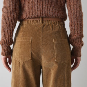 K&ouml;nnte beinhalten: Braune Cordhose mit weitem Bein und zwei Ges&auml;&szlig;taschen. Die Hose hat einen braunen G&uuml;rtel und einen Kordelzugbund.