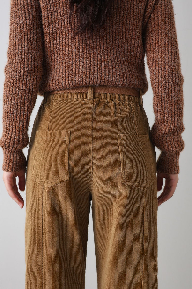 K&ouml;nnte beinhalten: Braune Cordhose mit weitem Bein und zwei Ges&auml;&szlig;taschen. Die Hose hat einen braunen G&uuml;rtel und einen Kordelzugbund.