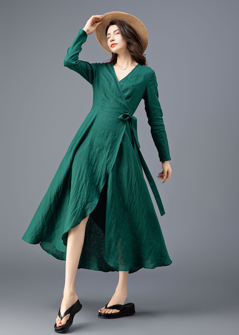 May include: A green wrap dress with long sleeves and a tie at the waist. The dress has a high low hemline and is made of a lightweight fabric.