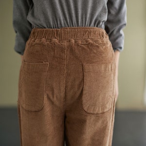May include: Brown corduroy trousers with two large pockets at the back. The trousers have an elastic waistband.