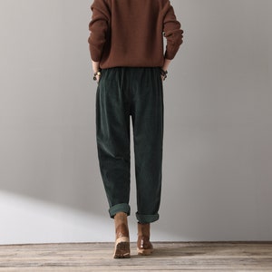 May include: A pair of dark green corduroy pants with a wide leg and a relaxed fit. The pants have a drawstring waistband and are cuffed at the ankles.