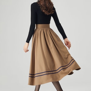 May include: A brown midi skirt with a high waist and two navy blue stripes around the hem. The skirt is made of a soft, flowing fabric and has a flattering A-line silhouette.