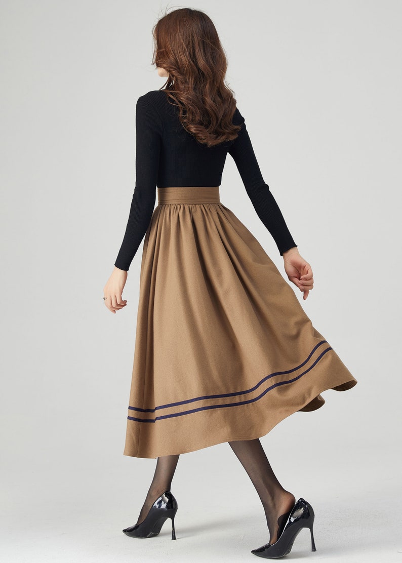 May include: A brown midi skirt with a high waist and two navy blue stripes around the hem. The skirt is made of a soft, flowing fabric and has a flattering A-line silhouette.