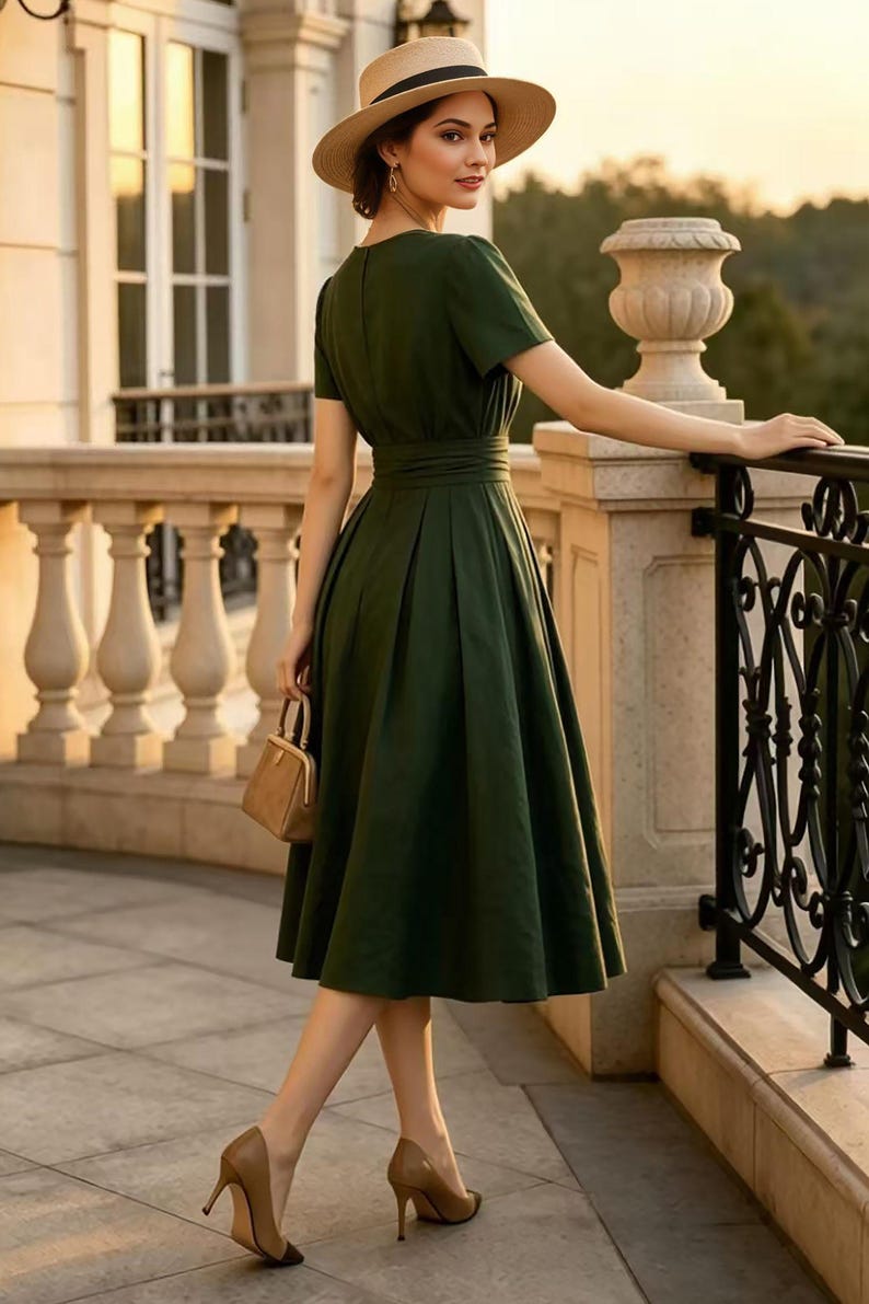 May include: A dark green midi dress with short sleeves, a fitted waist, and a pleated skirt. The outfit includes a tan straw hat with a black band, tan high-heeled pumps, and a small tan handbag with a gold-tone metal frame and clasp closure.