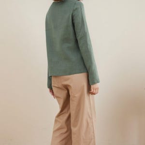 May include: A woman wearing a long-sleeved, sage green shirt and beige wide-leg pants.
