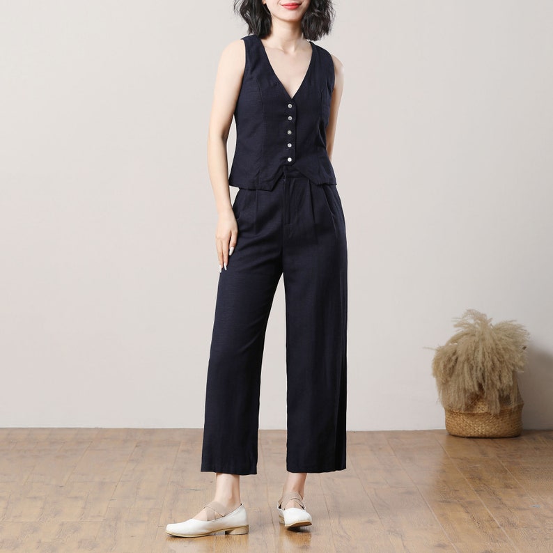 May include: A black sleeveless vest with a V-neckline and button closure, paired with wide-leg black trousers. The outfit is made of a lightweight fabric.