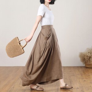 May include: A brown linen skirt with a high waist and a large pocket on the front. The skirt is flowing and has a relaxed fit.