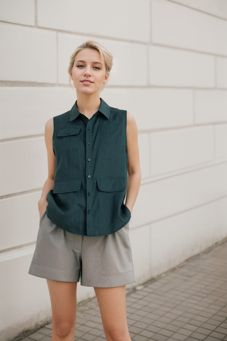 May include: A woman wearing a dark green sleeveless button-up shirt with two pockets and gray shorts.