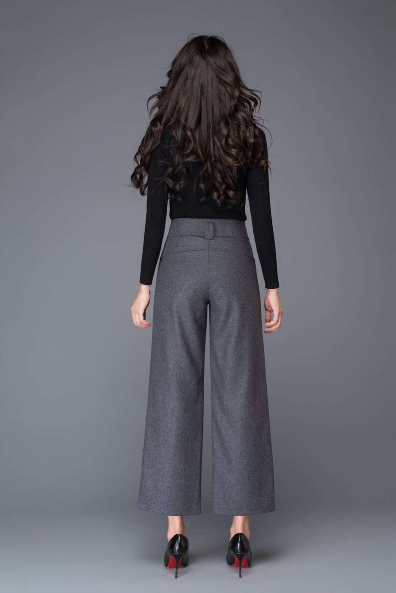 Puede incluir: Una mujer con una camisa negra de manga larga y pantalones grises anchos con cintur&oacute;n. Lleva tacones negros con suelas rojas.