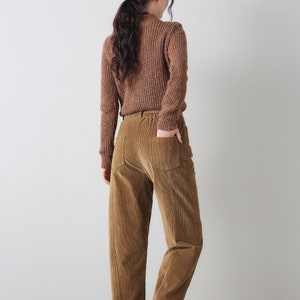 K&ouml;nnte beinhalten: Eine braune Cordhose mit lockerer Passform und elastischem Bund. Die Hose hat eine leicht verk&uuml;rzte L&auml;nge und wird an einem Model gezeigt, das einen braunen Pullover tr&auml;gt.