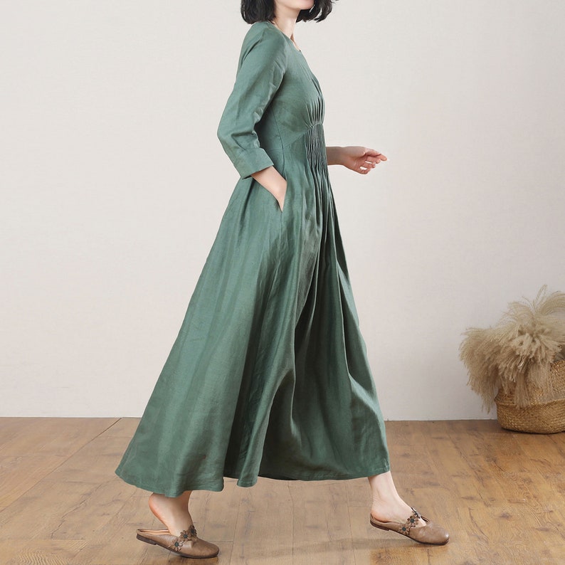 May include: A long, flowing green linen dress with a gathered waist and three-quarter sleeves. The dress has a simple, elegant design and is perfect for a variety of occasions.
