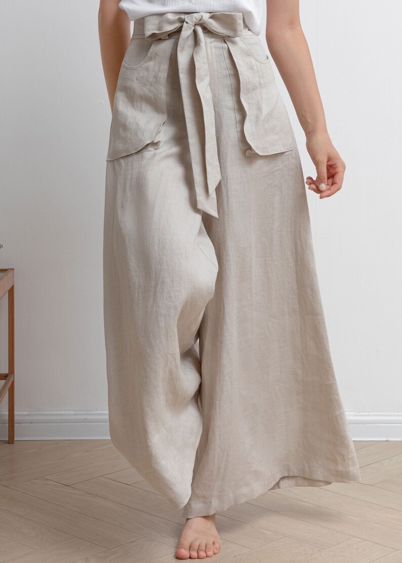 May include: Wide-leg linen pants with a tie belt and large pockets. The pants are a light beige color.