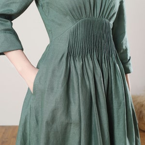 May include: A green linen dress with a pleated bodice and pockets. The dress has a relaxed fit and a midi length.