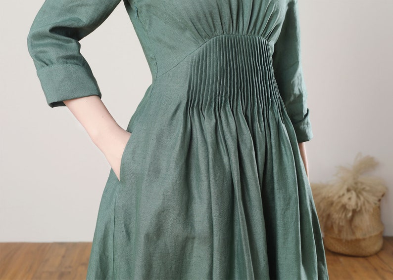 May include: A green linen dress with a pleated bodice and pockets. The dress has a relaxed fit and a midi length.