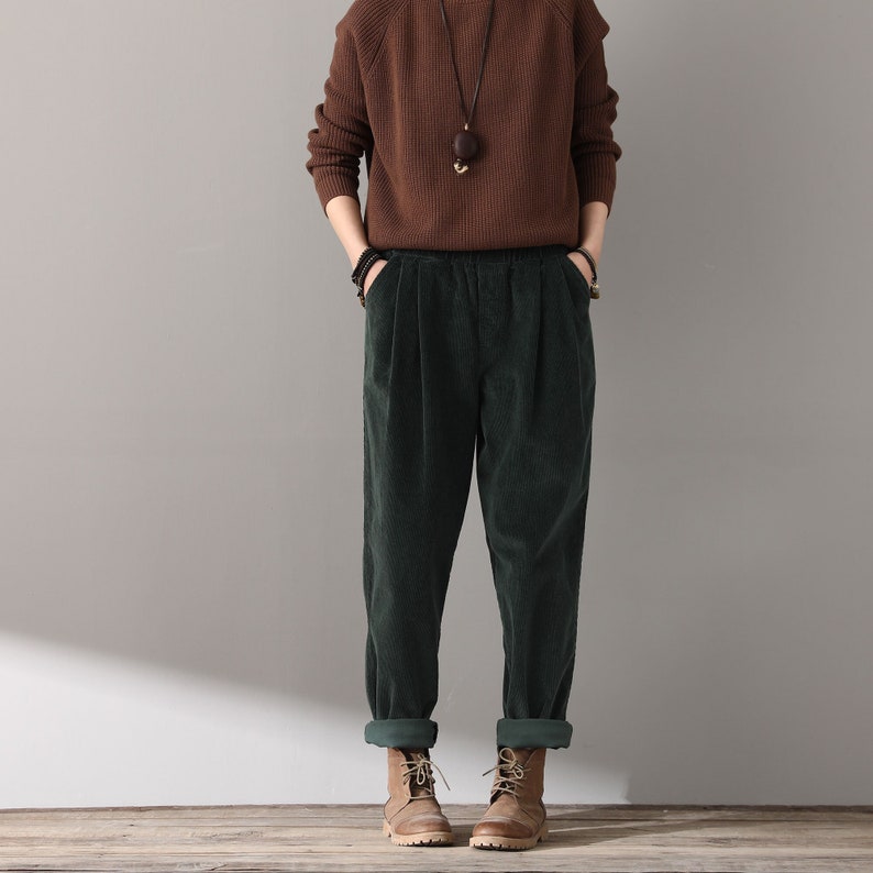 May include: Green corduroy pants with a high waist and a relaxed fit. The pants have a cuffed hem and are worn with brown boots.