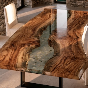 May include: A rectangular dining table featuring two thick slabs of natural brown wood with prominent grain patterns, separated by a central translucent resin river inlay. The table is supported by a black metal frame base and has a glossy finish.