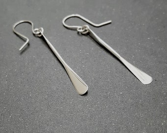 Può includere: Un paio di orecchini pendenti in argento con un design semplice, allungato a forma di pagaia.