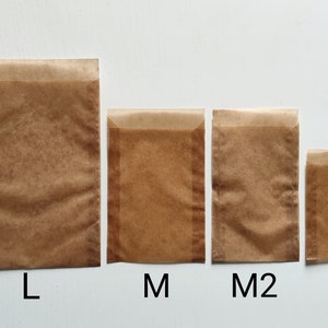 May include: Four brown paper bags in different sizes labeled L, M, M2, and S. The bags are made of a translucent, waxed paper.