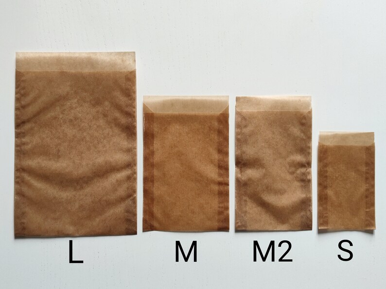 May include: Four brown paper bags in different sizes labeled L, M, M2, and S. The bags are made of a translucent, waxed paper.