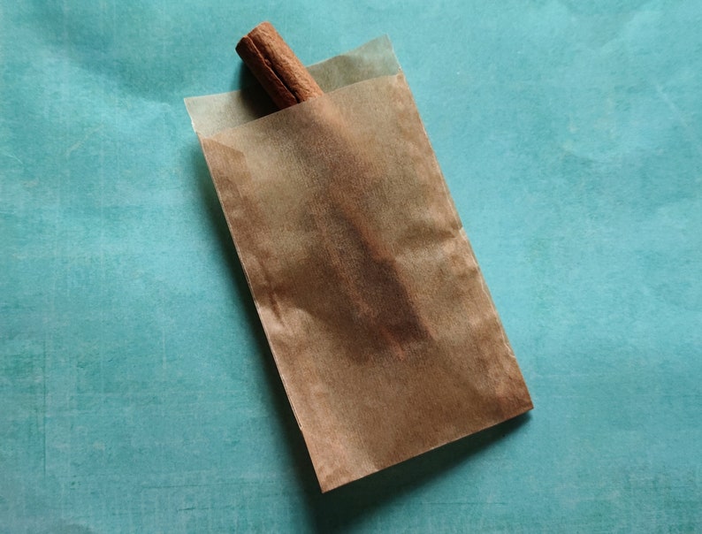 May include: A brown paper bag with a cinnamon stick inside. The bag is on a teal blue surface.