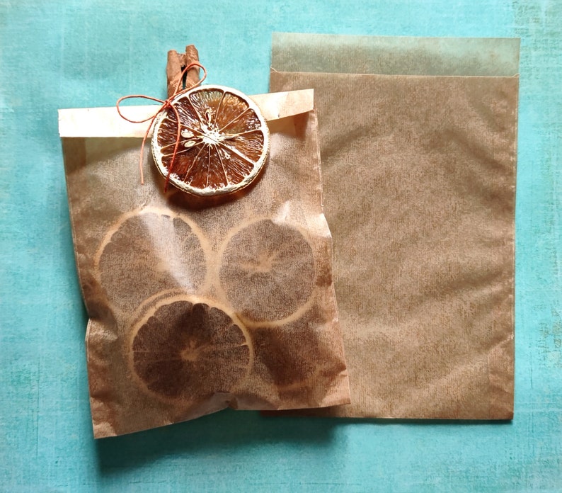 May include: Two brown paper bags with dried orange slices inside. The bags are tied with twine and a cinnamon stick.