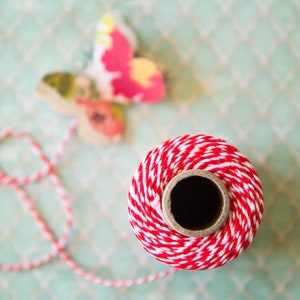 May include: A spool of red and white baker's twine with a butterfly decoration on a green patterned surface.