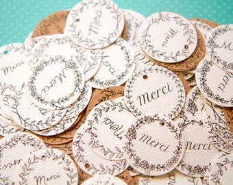 Può includere: Una collezione di etichette rotonde con la parola "Merci" in elegante corsivo. Ogni etichetta è adornata da un delicato design a ghirlanda floreale e di foglie in inchiostro nero. Alcune sono bianche sporco, altre marroni.