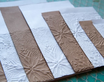 Könnte beinhalten: Ein Satz von sechs geprägten Papierkarten mit einem Schneeflockenmuster. Die Karten sind in abwechselnden Farben Weiß und Braun.