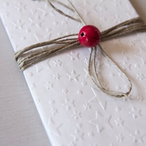 May include: A white card with a star pattern is tied with twine and a red bead.