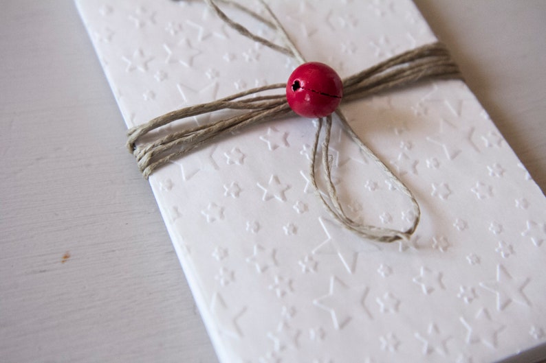 May include: A white card with a star pattern is tied with twine and a red bead.