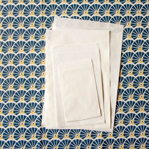 May include: A set of four white envelopes of different sizes, stacked on top of each other. The envelopes are on a blue and yellow patterned background.