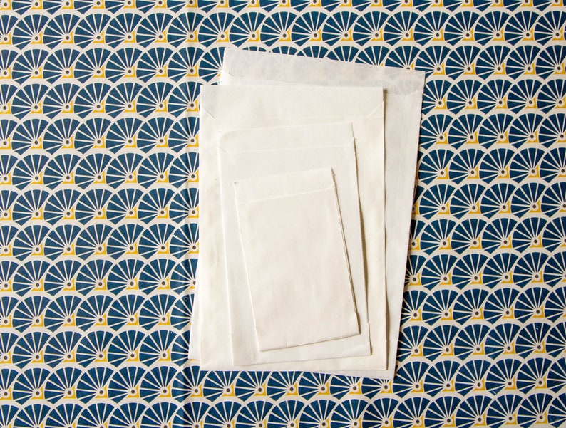 May include: A set of four white envelopes of different sizes, stacked on top of each other. The envelopes are on a blue and yellow patterned background.