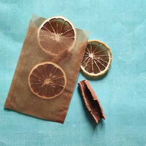 May include: Three dried orange slices and a cinnamon stick on a blue background. The orange slices are arranged in a semi-circle, with the cinnamon stick in the center.
