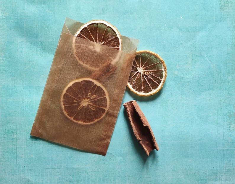 May include: Three dried orange slices and a cinnamon stick on a blue background. The orange slices are arranged in a semi-circle, with the cinnamon stick in the center.