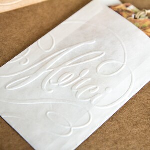 May include: White paper gift bag with the word "Merci" embossed in a cursive font.