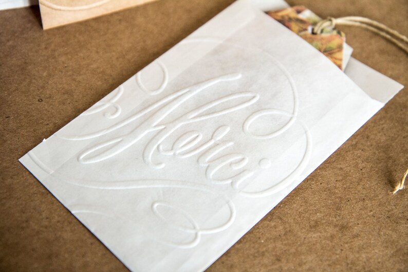 May include: White paper gift bag with the word "Merci" embossed in a cursive font.