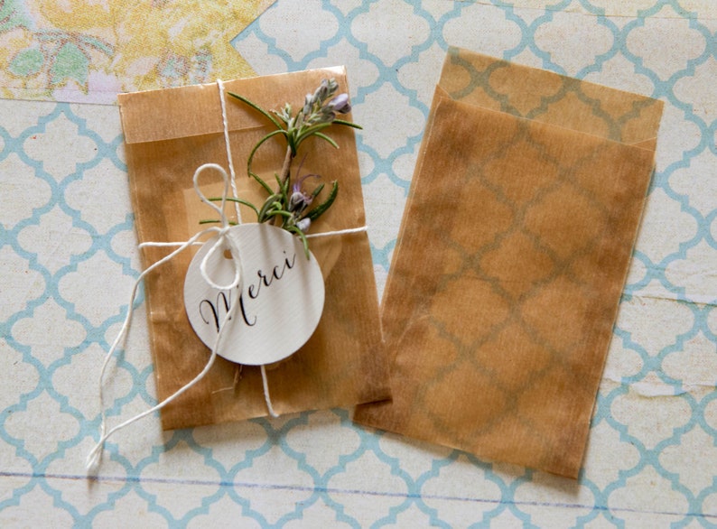 May include: Two brown paper bags, one tied with twine and a white tag that says "Merci", and the other is empty. Both bags are on a blue and white patterned surface.
