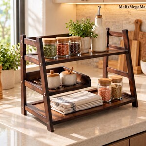 May include: A dark brown wooden tiered spice rack with three shelves. The top shelf holds three glass jars with wooden lids and a white ceramic oil dispenser. The middle shelf holds two small ceramic bowls. The bottom shelf holds a folded linen towel.
