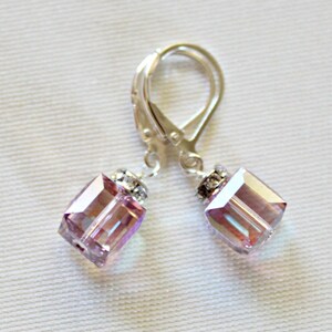 May include: A pair of silver earrings with a light purple square crystal dangle. The crystals have a iridescent finish.