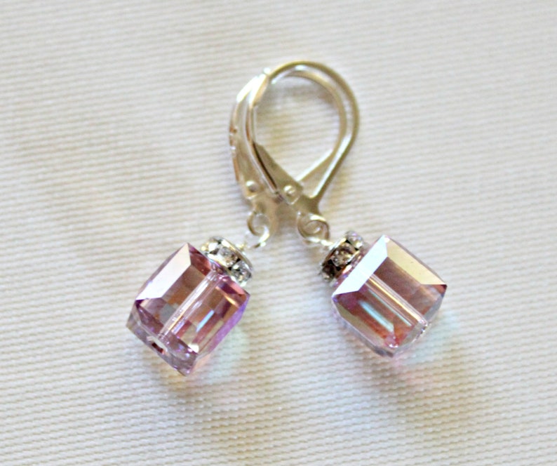 May include: A pair of silver earrings with a light purple square crystal dangle. The crystals have a iridescent finish.