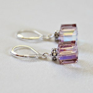 May include: A pair of silver earrings with a light purple crystal dangle. The crystals are faceted and have a shimmery finish.