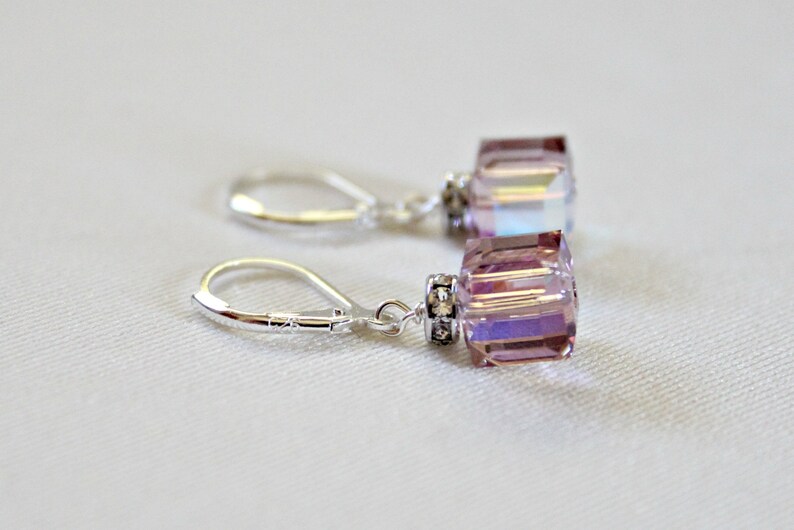 May include: A pair of silver earrings with a light purple crystal dangle. The crystals are faceted and have a shimmery finish.