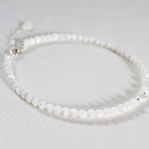 May include: A white pearl bracelet with a silver clasp. The bracelet is made of small, round pearls and has a delicate, feminine look.