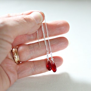 May include: A pair of silver dangle earrings with red teardrop-shaped crystals.