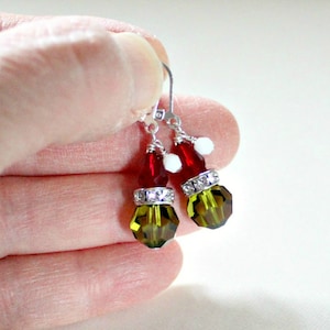 May include: A pair of dangle earrings with a red and green crystal design. The earrings feature a red crystal, a white crystal, and a green crystal with rhinestones.