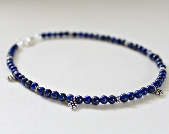 May include: A blue lapis lazuli beaded bracelet with silver flower charms.