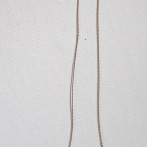 May include: A silver chain necklace with three heart-shaped stones. The stones are green, pink, and green. The necklace is about the size of a US penny.