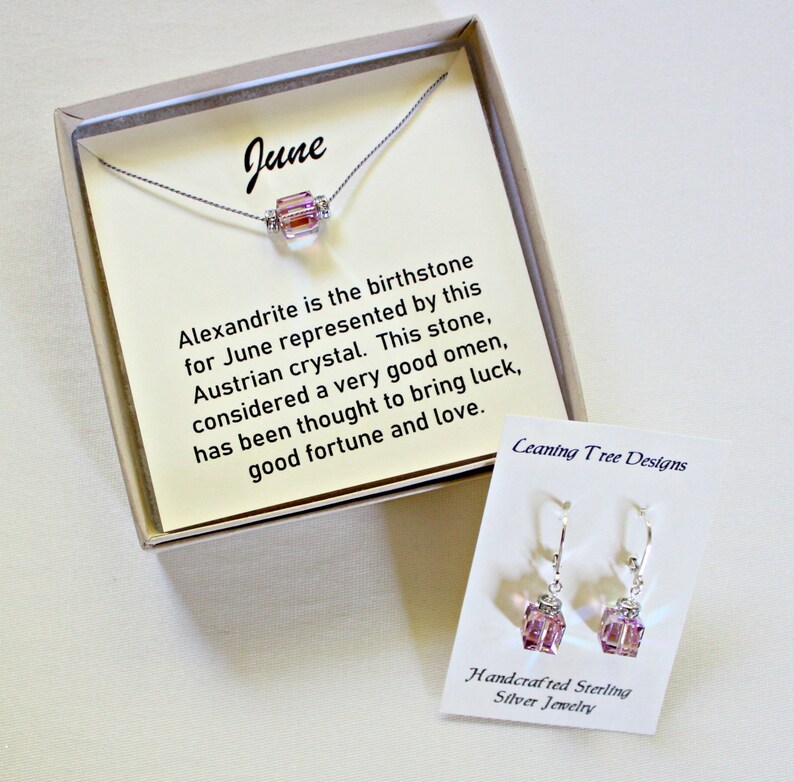 May include: A gift box containing a silver necklace with a pink alexandrite crystal pendant and a pair of matching earrings. The box includes a card that reads "June" and describes the alexandrite as the birthstone for June, considered a good omen to bring luck, good fortune, and love. The card also includes the text "Ceaning Tree Designs". The earrings are labeled "Handcrafted Sterling Silver Jewelry".